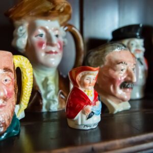 A collection of vintage ceramic character mugs displayed on a shelf.